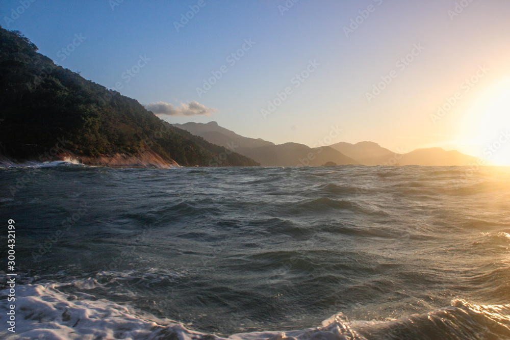 Atlantic ocean with rippling water and sea foam and mountains at sunset. Landscape with the beach of Brazil on the island of Ilha Grande.