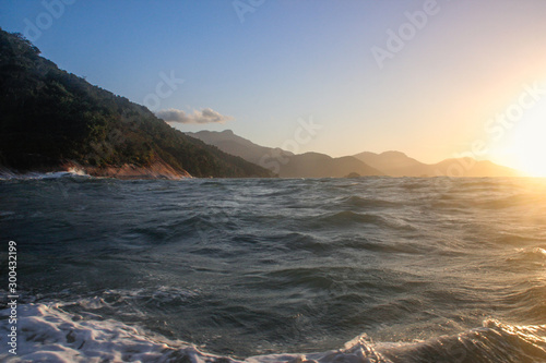Atlantic ocean with rippling water and sea foam and mountains at sunset. Landscape with the beach of Brazil on the island of Ilha Grande. photo