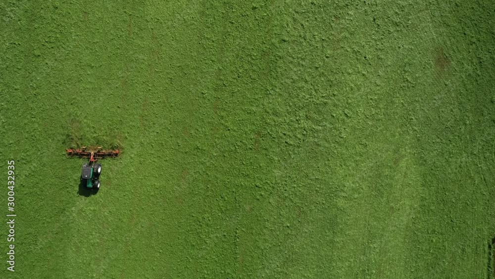 Aerial top-down view of green grass farm field with tractor raking ...