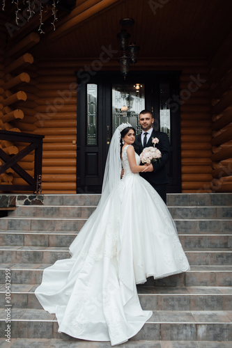 Stylish couple of happy newlyweds posing walking up the stairs on their wedding day. Perfect couple bride  groom posing and hugging. Wedding dress. Bridal wedding bouquet of flowers