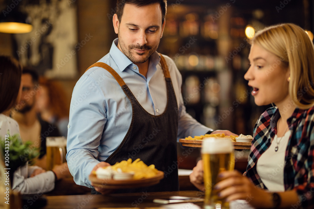Smiling waiter serving tortilla chips to a woman in a pub. Smiling waiter serving tortilla chips to a woman in a pub.