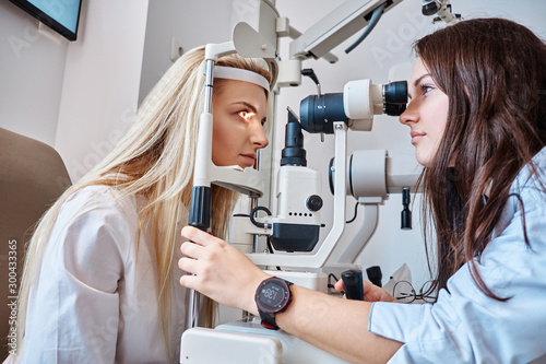 Female patient on eyesight test at optician cabinet with young female oculist.