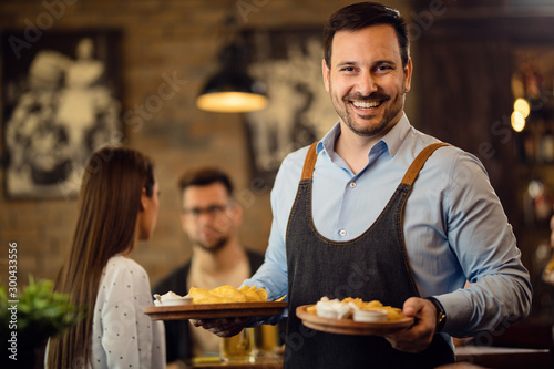 Happy waiter holding plates with food and looking at camera in a pub. photo