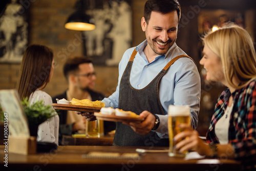 Happy waiter giving nachos to a woman who is drinking beer in a pub. photo