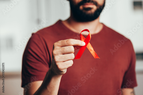 Man holding red ribbon for HIV illness awareness, 1 December World AIDS Day concept.