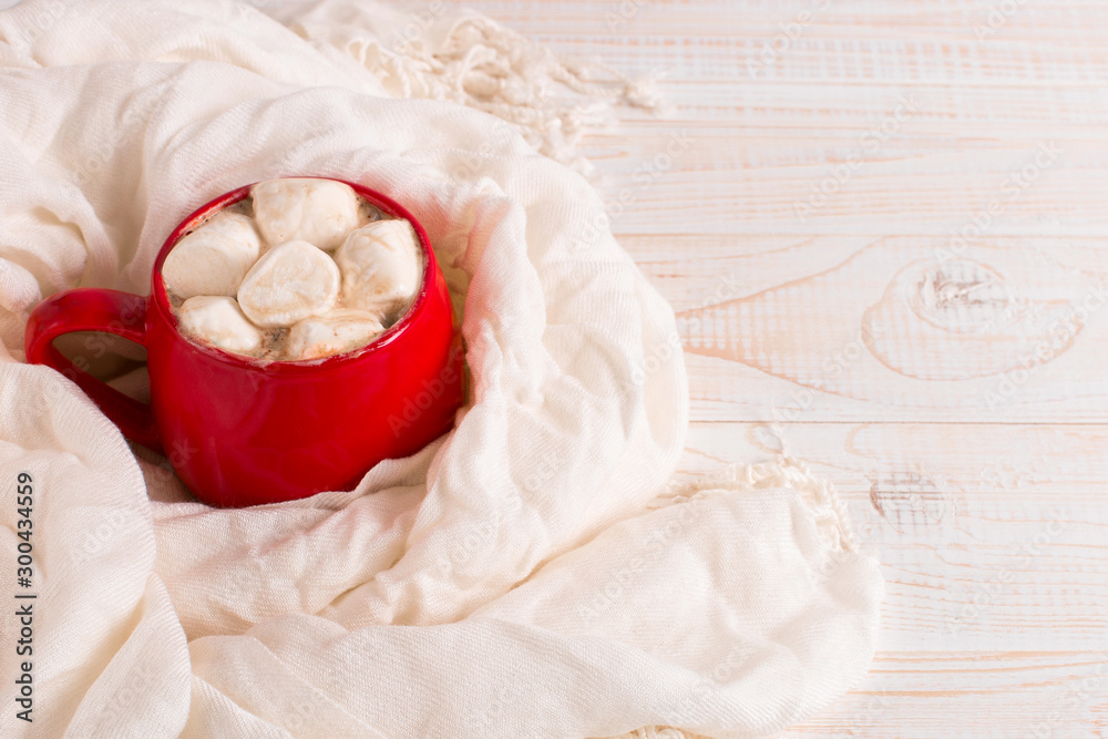 Obraz premium Red mug with cocoa and marshmallows on a white table scarf background. Autumn mood, a warming drink. Copy space.
