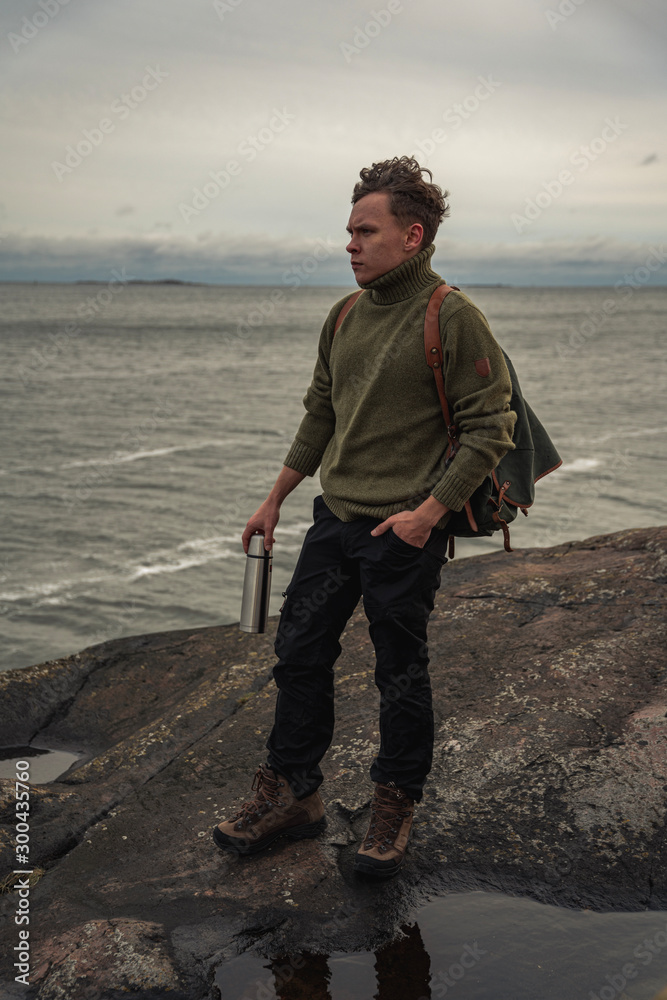 Young man standing on beach made of bedrock, arhchipelago and the sea in the background