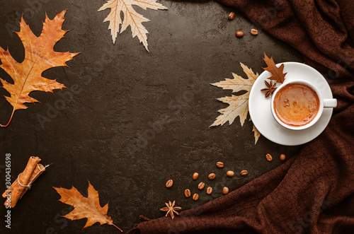 Autumn flat lay. Cup of coffee, brown pashmina scarf, autumn leaves, cinnamon sticks and coffee beans on black background. Top view. Copy space