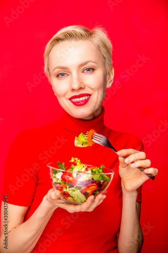  Beautiful caucasian woman eating salad over red background. studio shot