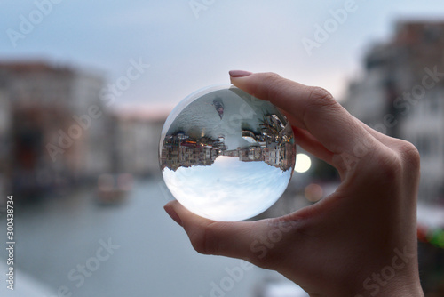 A hand holding a glass sphere with the reflection of the Grand Canal of Venice inside shooted from the Rialto bridge