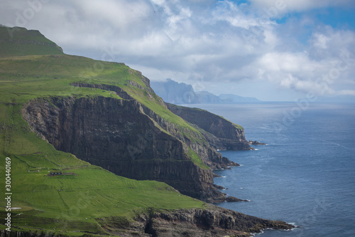 View on the Mykines island with moody clouds covering the top of the mountains and sheep grazing on the pasture, Mykines island, Faroe Islands, Europe.