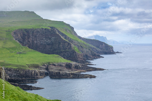 View on the Mykines island with moody clouds covering the top of the mountains and sheep grazing on the pasture, Mykines island, Faroe Islands, Europe.
