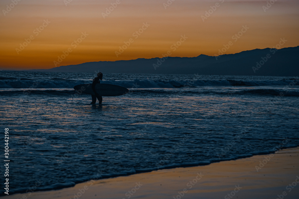Sunset on the Pacific Coast in California, surfer and joggers run a sport