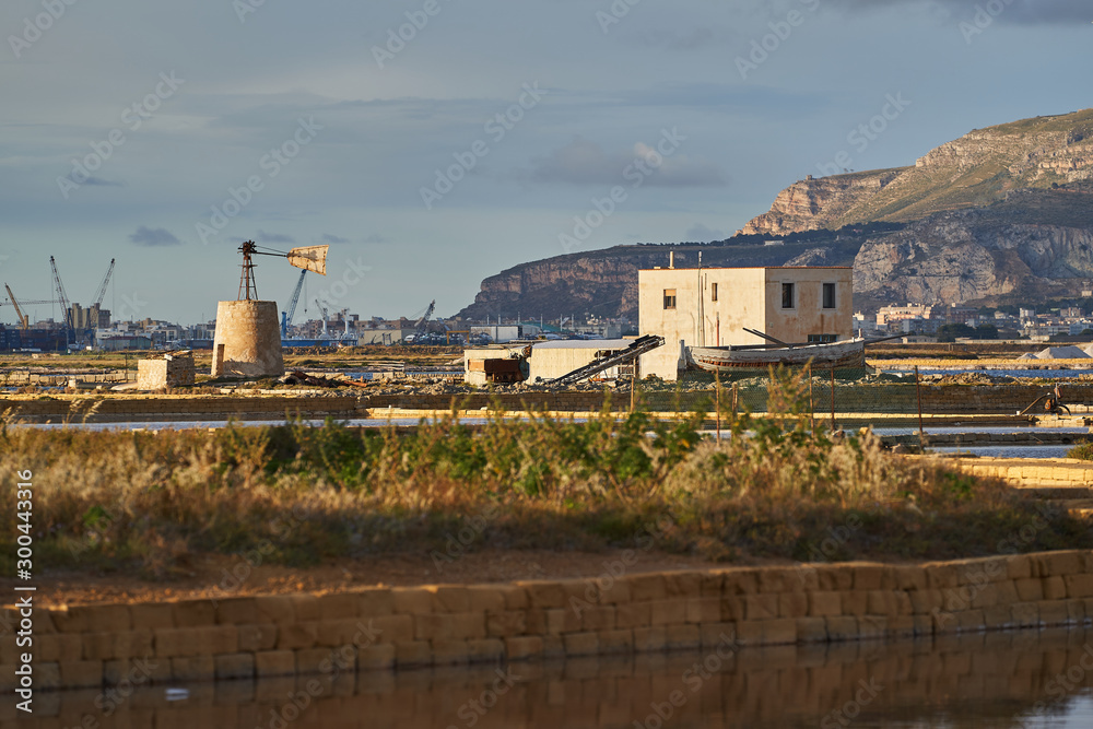 Landscape picture of saltpans in traditional salt production close to sicilian city Trapani in italy, historical architecture like water lifting mill, old barrages and shallow ponds with sea water.