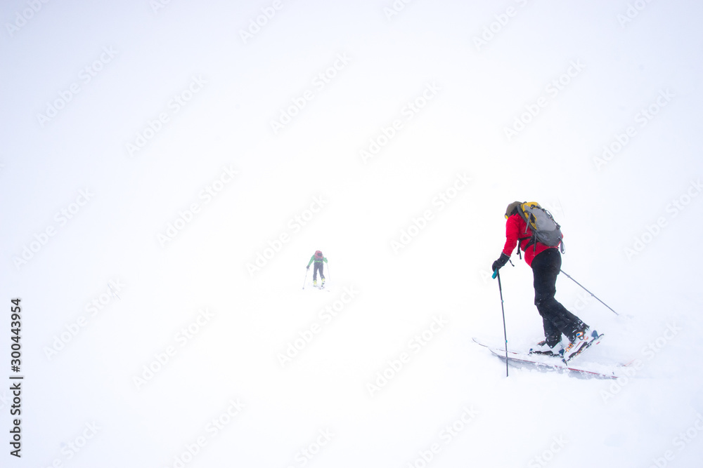 Two skiers struggling into a snow storm during a whiteout in the mountains Two skiers struggling into a snow storm during a whiteout in the mountains