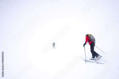 Obraz na plátne Two skiers struggling into a snow storm during a whiteout in the mountains