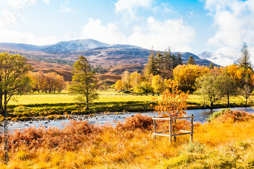 Autumn in Glen Strathfarrar in the Scottish Highlands. Landscape with snow topped mountains, pine trees, golden ferns and the River Farrar running through the Glen. Horizontal. Space for copy..