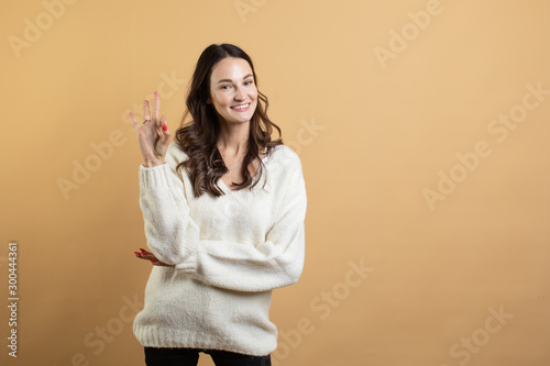 An image of a young beautiful woman in a white sweater posing on an isolated orange background shows different emotions