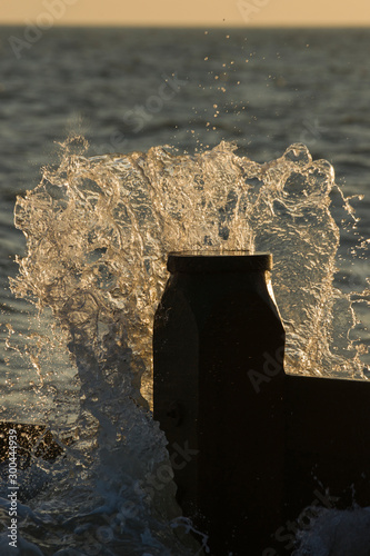 A Wave breaks over a groyne at sunset taken on Southwick Beach, West Sussex, United Kingdom. photo