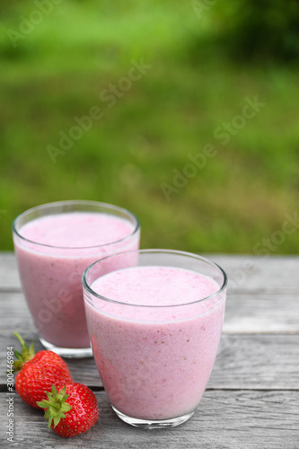A glass of fresh cold smoothie with berries and cherrys on a wooden table, summer set, outdoor greed blured background,boke.