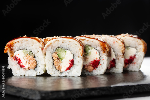 Golden dragon sushi roll. Sushi Rolls with flying fish caviar , tuna, eel, cucumber, sesame seeds and Cream Cheese inside and on black slate isolated. Horizontal