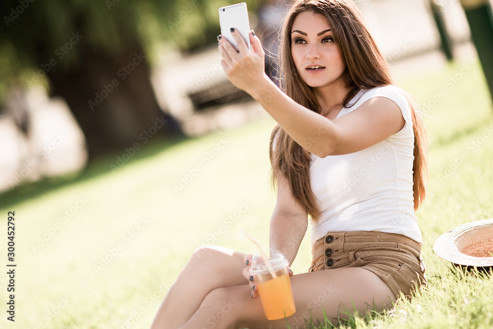 Beautiful young woman sitting on grass and using phone in summer park. Beautiful young woman sitting on grass and using phone in summer park.
