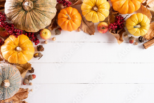 Top view of  Autumn maple leaves with Pumpkin and red berries on white wooden background. Thanksgiving day concept.