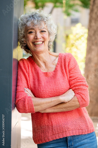 beautiful older woman leaning against wall smiling with arms crossed outdoors