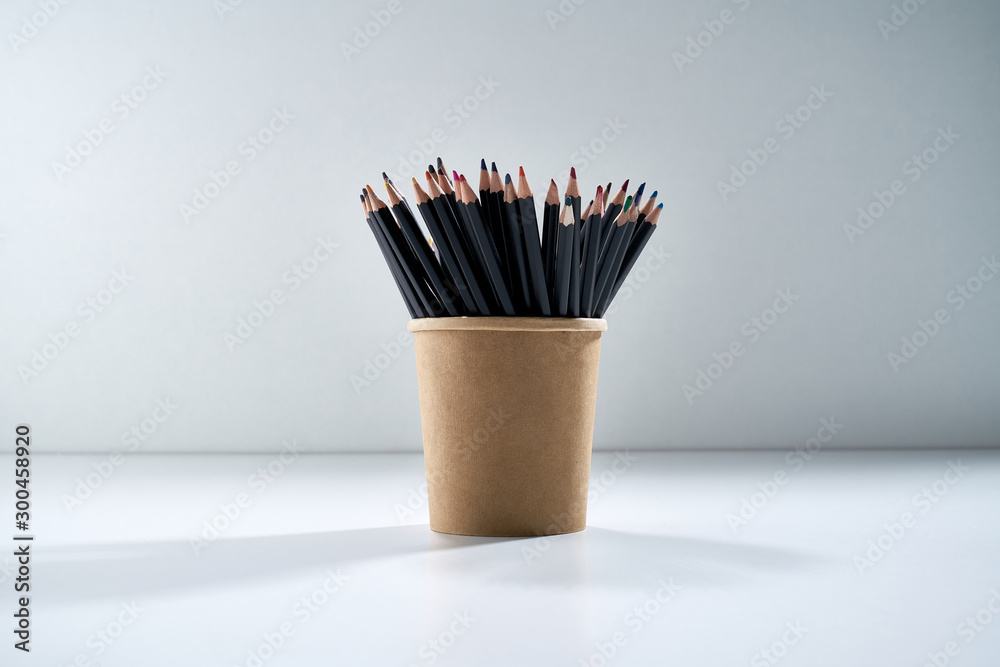 Multi-colored pencils for drawing in a brown cardboard stand on a gray background