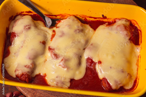 Delicious Chicken Parmigiana served in yellow baking dish with on a wooden table and stone or concrete background..