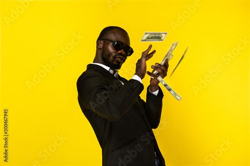 Handsome afroamerican guy scatters money and looks selfish