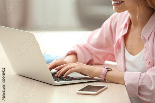 Young woman using laptop at table indoors, closeup