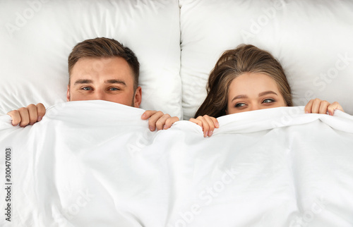 Young couple hiding under blanket together, top view. Bedtime
