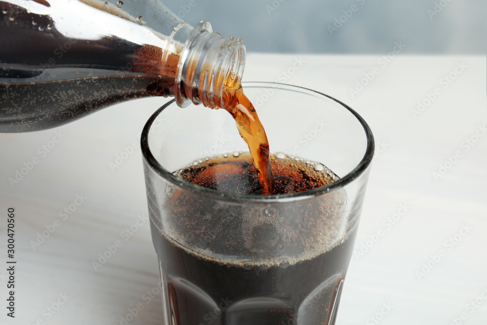Pouring refreshing soda drink into glass on table, closeup - obrazy, fototapety, plakaty 