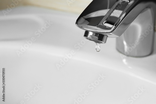 Closeup view of water dropping from faucet indoors. Space for text