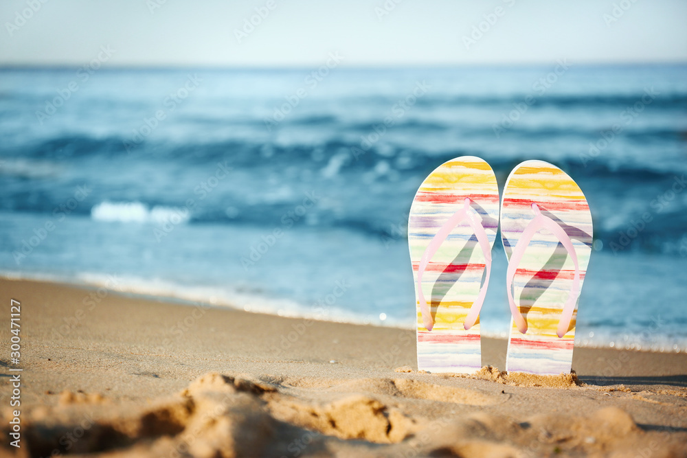 Stylish flip flops on sand near sea, space for text. Beach accessories - obrazy, fototapety, plakaty 