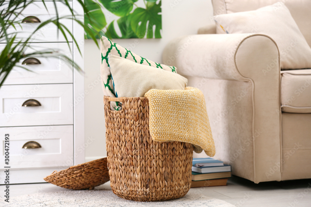Basket with soft plaid and pillows in living room interior - obrazy, fototapety, plakaty 
