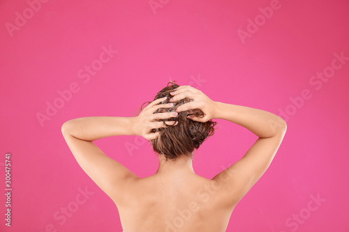 Young woman washing hair on pink background