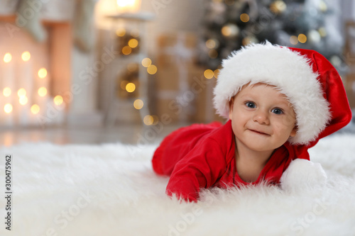 Little baby wearing Santa hat on floor at home. First Christmas
