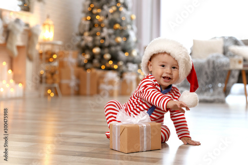 Little baby with Santa hat and Christmas gift on floor at home photo