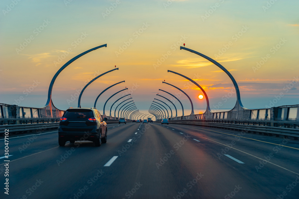 Obraz premium Expressway. Traffic on the bridge. Cars go against the background of the setting sun. Road infrastructure. Travel by car. Road home. Motorway in the evening.