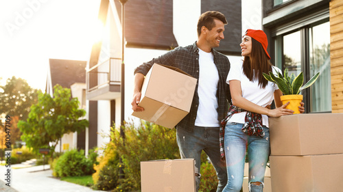 Fotografie Happy couple with moving boxes and household stuff near their new house on sunny