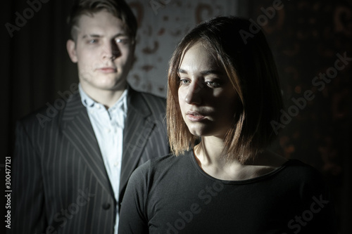A man and a girl in dark clothes on a dark background. Problem in relations. Incomprehension. Alienation. Divorce. Lack of joy from communication. Sadness. photo