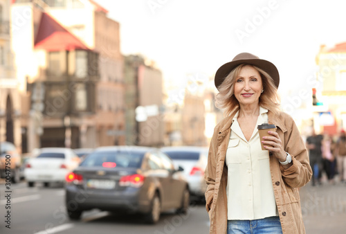 Mature woman with cup of coffee on city street © New Africa