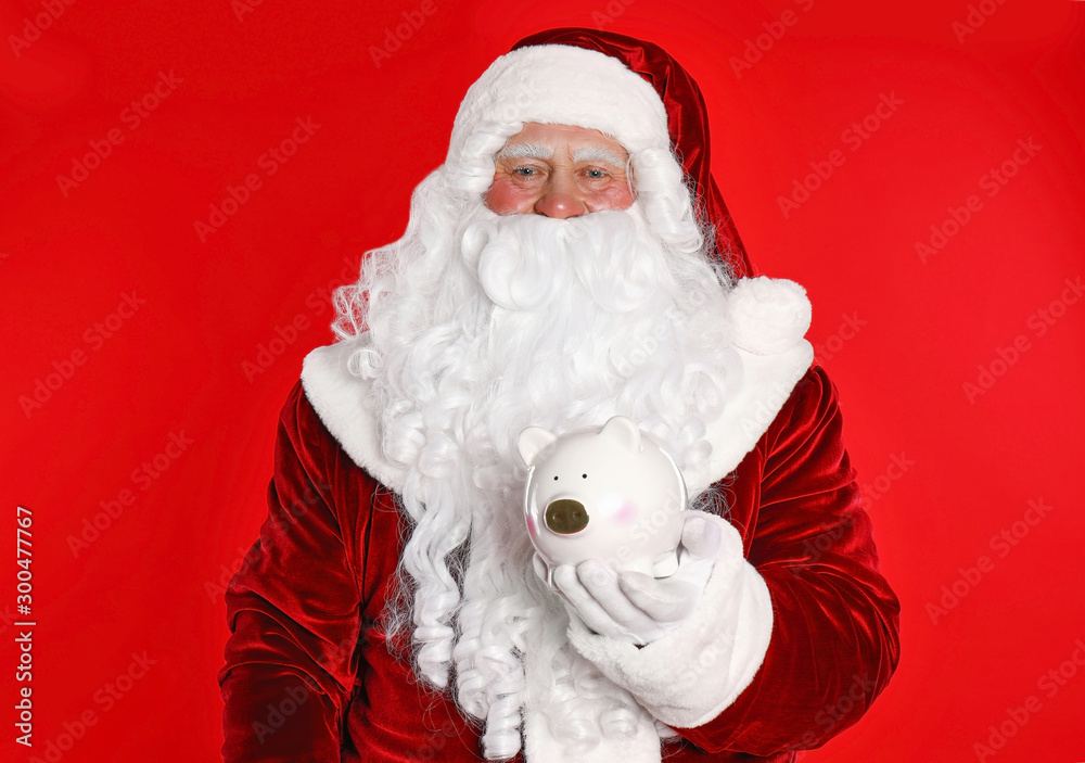 Santa Claus holding piggy bank on red background Santa Claus holding piggy bank on red background