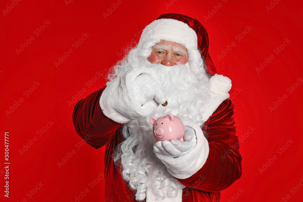 Santa Claus putting coin into piggy bank on red background Santa Claus putting coin into piggy bank on red background