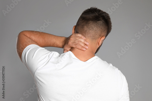 Man suffering from neck pain on light grey background