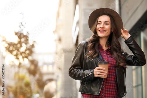 Beautiful woman with cup of coffee on city street. Autumn walk