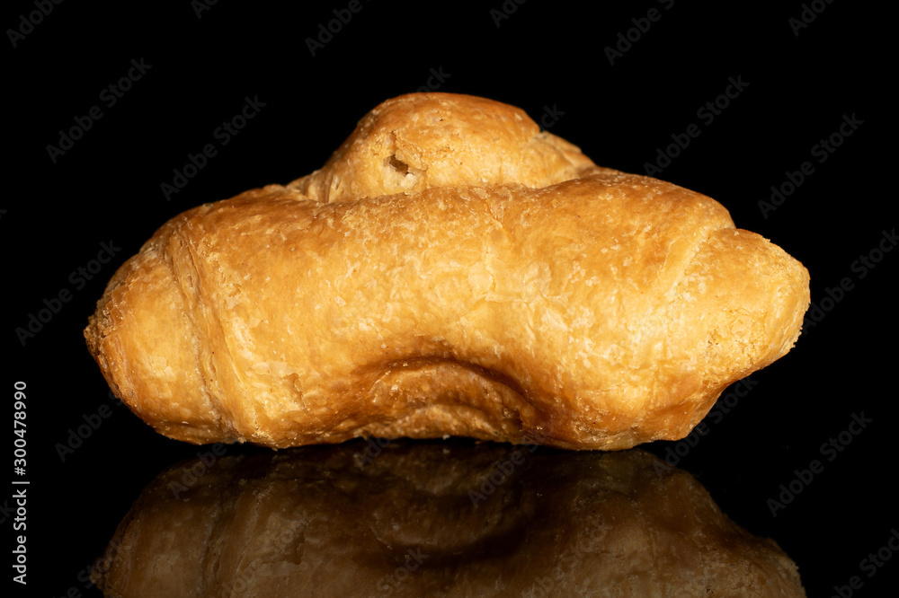 One whole fresh baked mini croissant isolated on black glass One whole fresh baked mini croissant isolated on black glass
