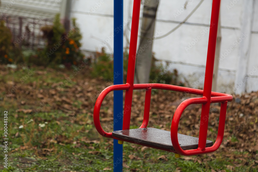 Empty children's swing red color close-up. The concept of sadness, loss, death, mourning, orphanhood or loneliness.